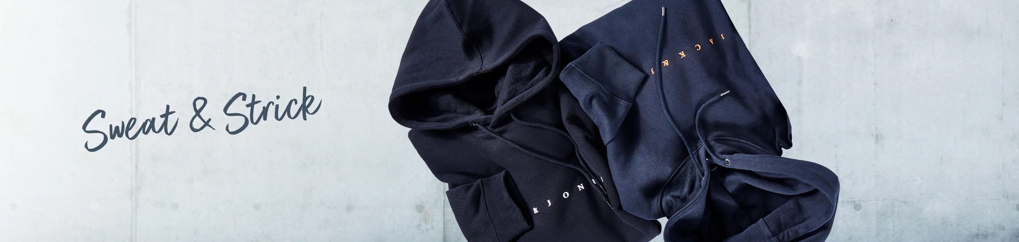 Dunkelblaue Kapuzenpullover von Jack & Jones locker arrangiert vor Betonwand – moderne Sweats für Männer mit Format.